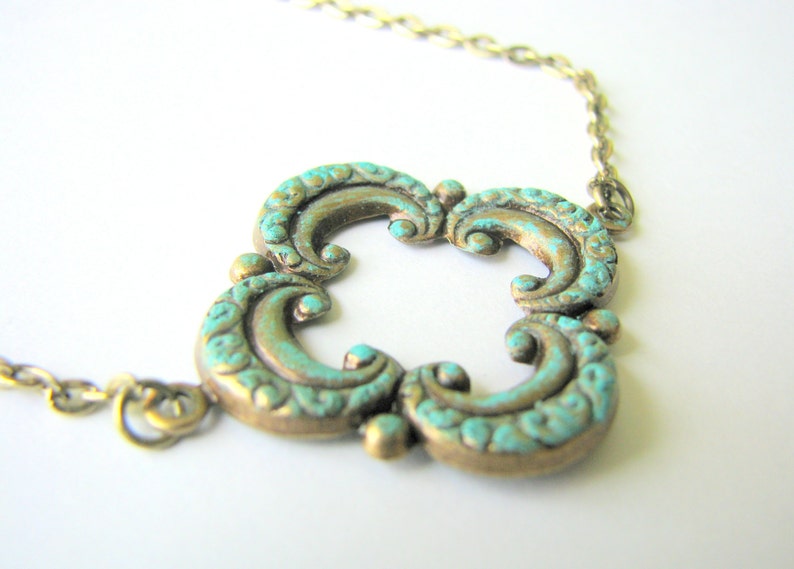 May include: A turquoise and gold necklace with a decorative, ornate pendant. The pendant is shaped like a four-leaf clover with a detailed, swirling design.