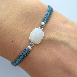 May include: A blue braided bracelet with a white, sparkly, rectangular charm.