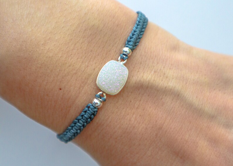May include: A blue braided bracelet with a white, sparkly, rectangular charm.