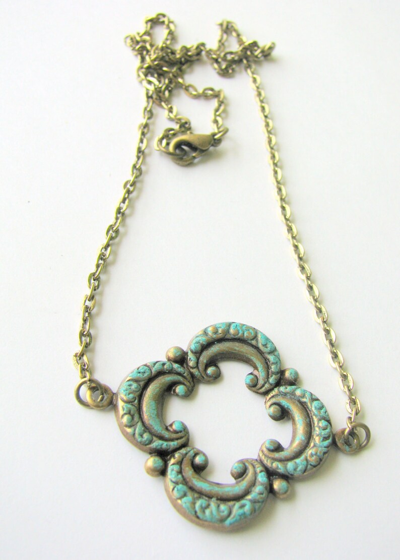 May include: A gold chain necklace with a turquoise and gold pendant featuring a quatrefoil design.