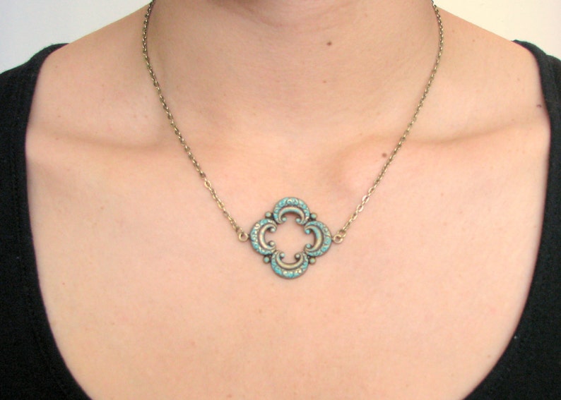 May include: A silver chain necklace with a turquoise blue pendant in the shape of a four-leaf clover.