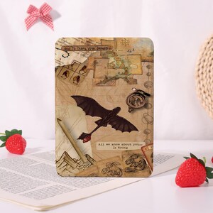 May include: A rectangular plaque featuring a collage of How to Train Your Dragon imagery, including a map, a compass, a pencil, and a black dragon in flight. The text reads "HOW TO TRAIN YOUR DRAGON" and "All we know about you... is Wrong".