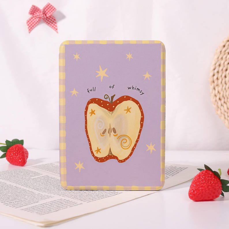 May include: A rectangular, lilac-coloured decorative sign featuring a whimsical apple illustration. The apple is halved, showing seeds and a swirl design. The text "full of whimsy" is above the apple. The sign has yellow stars and a yellow chequered border.