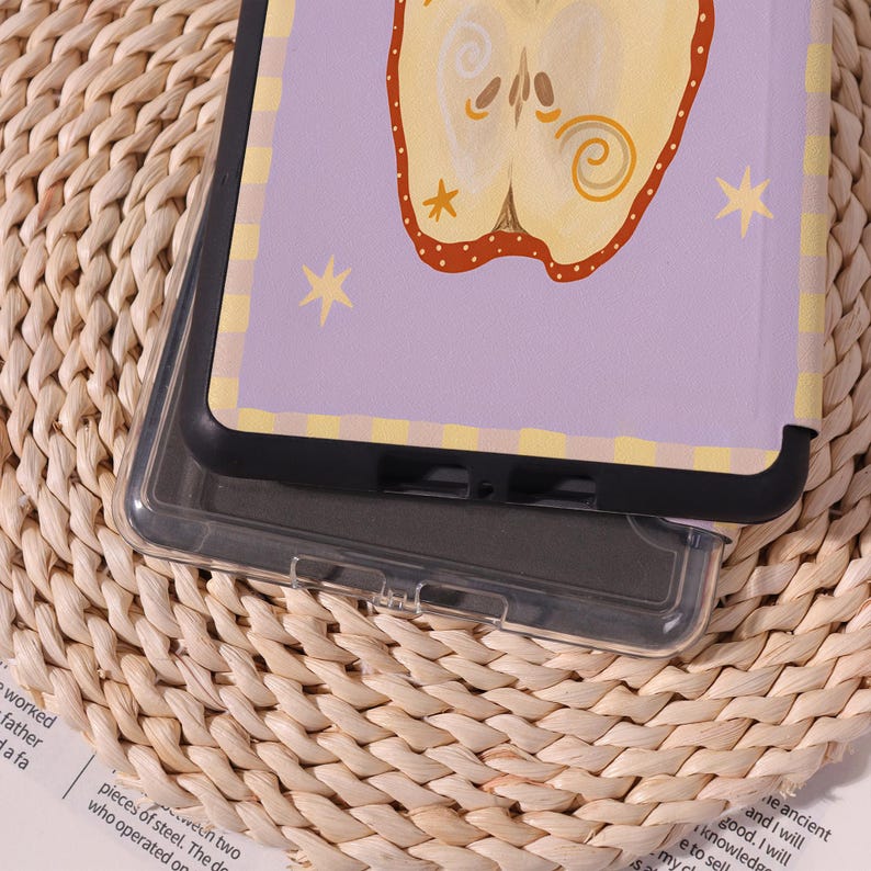 May include: A clear phone case with a purple and yellow design. The case features a stylized apple illustration with star accents. The case is resting on a woven surface.