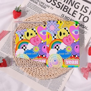 May include: Clear tablet case with a colorful design featuring smiley faces, hearts, rainbows, and flowers. The case has the words "GOOD DAY!" and "ALWAYS STAY POSITIVE" printed on it. The background is a mix of black and white checkerboard patterns.