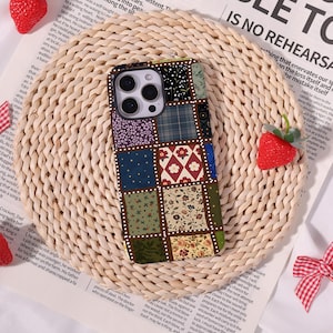 May include: A rectangular smartphone case featuring a patchwork design of various squares with floral, plaid, and geometric patterns in shades of blue, green, red, and cream, separated by thin white dotted lines, with a triple camera cutout at the top.