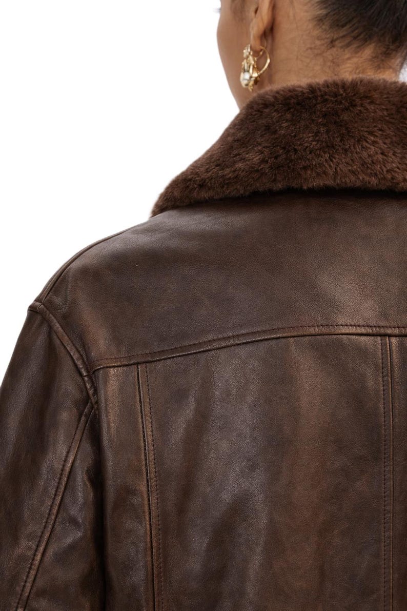 May include: A brown leather jacket with a faux fur collar. The jacket has a classic design with visible stitching details. The image shows the back of the jacket and part of the shoulder.