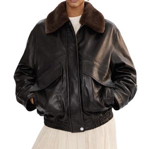 May include: A black leather bomber jacket with a brown faux fur collar. The jacket has two front pockets, a zipper closure, and a ribbed hem. The model is wearing a white top and a cream-colored skirt.