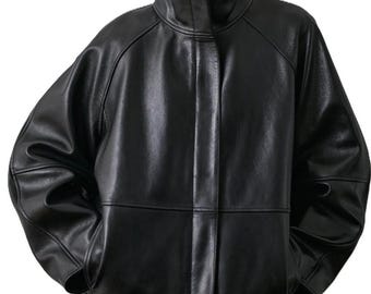 May include: A black leather jacket with a high stand-up collar, long sleeves, and a concealed front placket. The jacket features a smooth, semi-glossy finish, structured shoulder seams, and a loose, boxy fit that extends to the waistline.