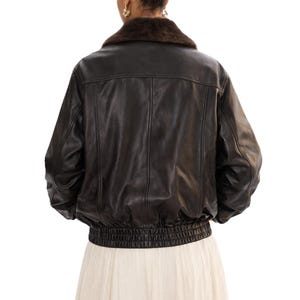 May include: A black leather jacket with a brown fur collar. The jacket has a ribbed elastic waistband and cuffs. The back of the jacket is visible, showing vertical seams and a classic bomber style.