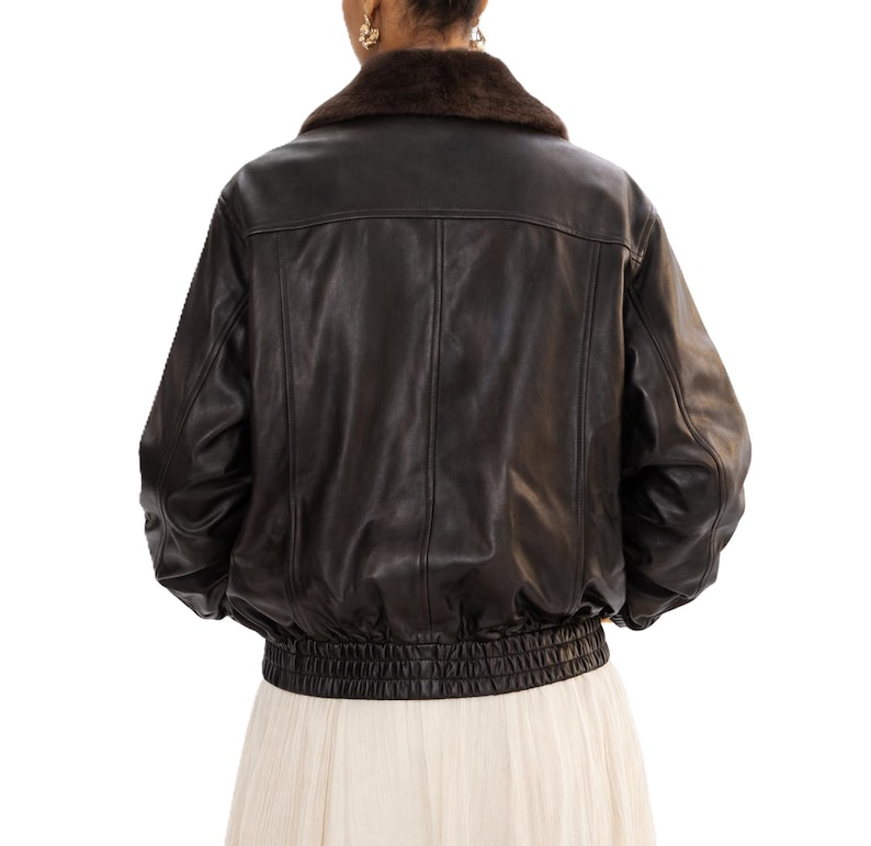May include: A black leather jacket with a brown fur collar. The jacket has a ribbed elastic waistband and cuffs. The back of the jacket is visible, showing vertical seams and a classic bomber style.