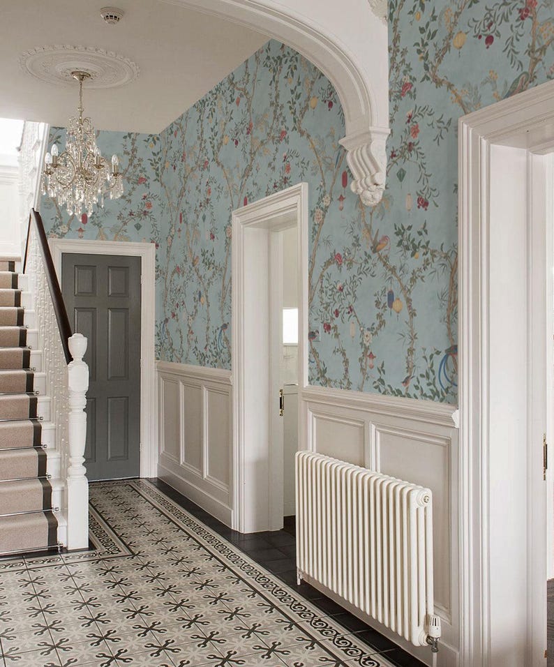 May include: An entryway with light blue floral wallpaper, white wainscoting, and a patterned tile floor. A crystal chandelier hangs from the ceiling. A gray door and staircase are visible.