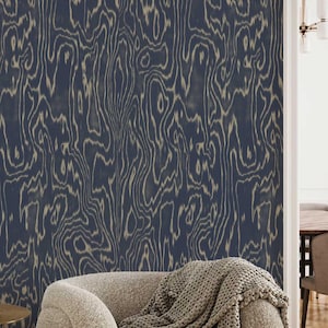 May include: Navy blue wallpaper with a wood grain pattern. The wallpaper is installed on a wall behind a beige armchair with a gray knitted throw. The room is partially visible, with a glimpse of a table and chairs.