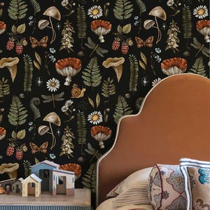 May include: A bedroom scene featuring a black wallpaper with a botanical pattern of mushrooms, ferns, and flowers. A brown headboard and a nightstand with wooden toy houses are in the foreground. Pillows and a quilt complete the cozy setting.