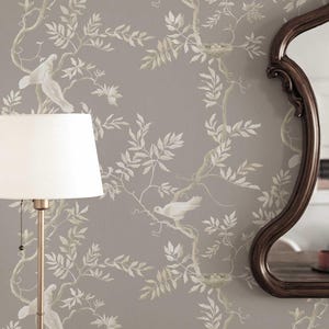 May include: Gray wallpaper with a repeating pattern of white birds, leaves, and branches. A gold floor lamp with a white lampshade is on the left. A brown, ornate mirror is on the right.