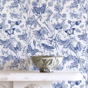 May include: A ceramic bowl sits on a white shelf against a backdrop of blue and white wallpaper. The wallpaper features a detailed botanical design with butterflies and flowers. The bowl has a textured, speckled appearance.