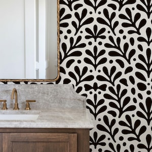 May include: A bathroom with a brown wooden vanity, a marble countertop, and a gold-framed mirror. The wall features a black and white floral pattern wallpaper. The faucet is gold-colored.