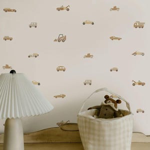 May include: A neutral-toned nursery scene featuring a white lamp with a pleated shade, a basket with a stuffed animal, and a wall decorated with car decals in shades of brown and beige. The overall theme is a child's room.