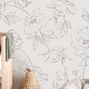 May include: A white wall with a large-scale floral pattern in black line art. The design features oversized peony blooms and leaves. A light-colored crib and a pear-shaped woven basket are in the foreground.