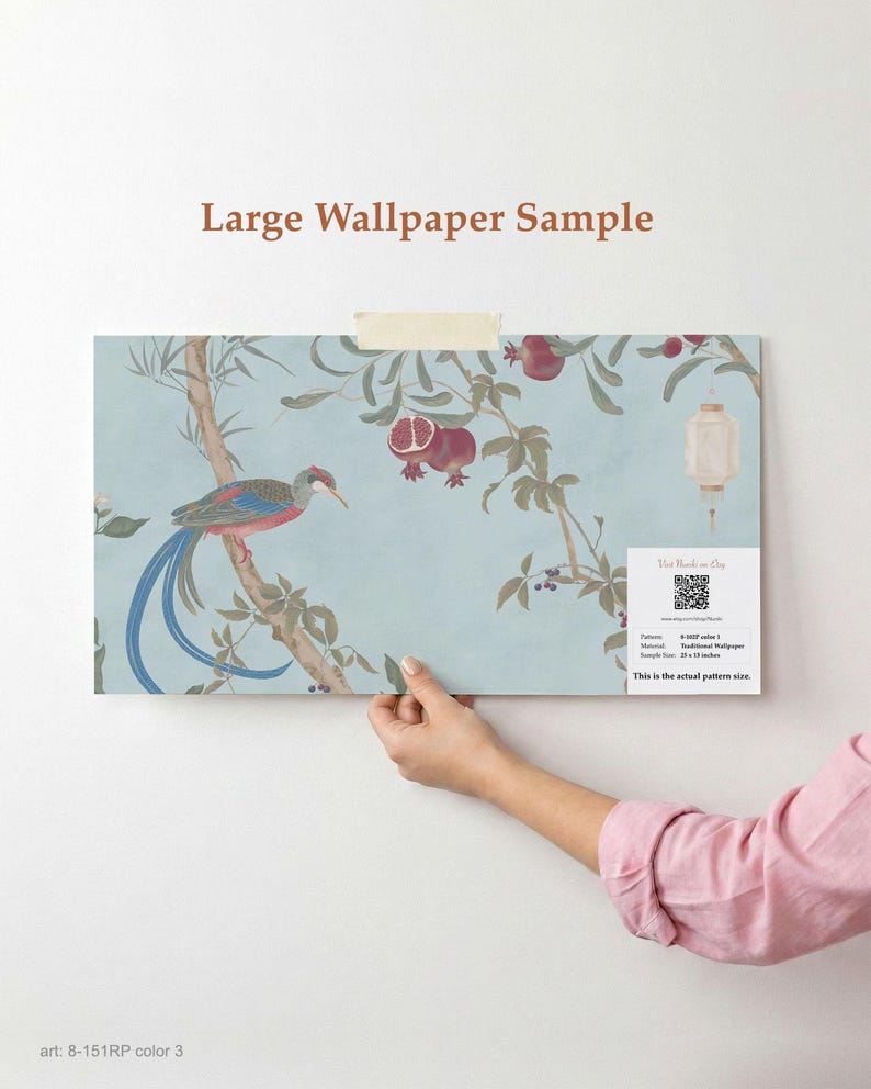 May include: A large wallpaper sample featuring a bird perched on a branch with pomegranates and a lantern against a light blue background. The sample is held up against a white wall. Text on the sample reads "Large Wallpaper Sample" and "This is the actual pattern size."
