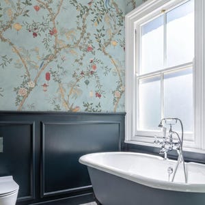 May include: A bathroom with a claw-foot bathtub, a window, and patterned wallpaper. The wallpaper features a light blue background with a floral and bird design. The bathtub is gray with a white interior.