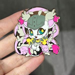 以下が含まれることがあります： 白い体、ピンクのアクセント、緑のヘルメットが特徴の漫画のキャラクターが描かれたカラフルなエナメルピン。 ピンは金色の縁取りがあり、手で持っています。 キャラクターは大きな青い目を持ち、黄色のオブジェクトを持っています。