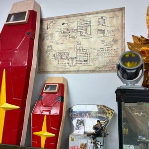 Könnte beinhalten: Rote und gelbe Schild-Requisiten mit einem rechteckigen Fenster, ausgestellt in der Nähe eines Vintage-Grundrisses eines Herrenhauses. Ein Batman-Themenlicht und eine Figur sind ebenfalls zu sehen, was auf eine Sammlung von Sammlerstücken und Erinnerungsstücken hindeutet.