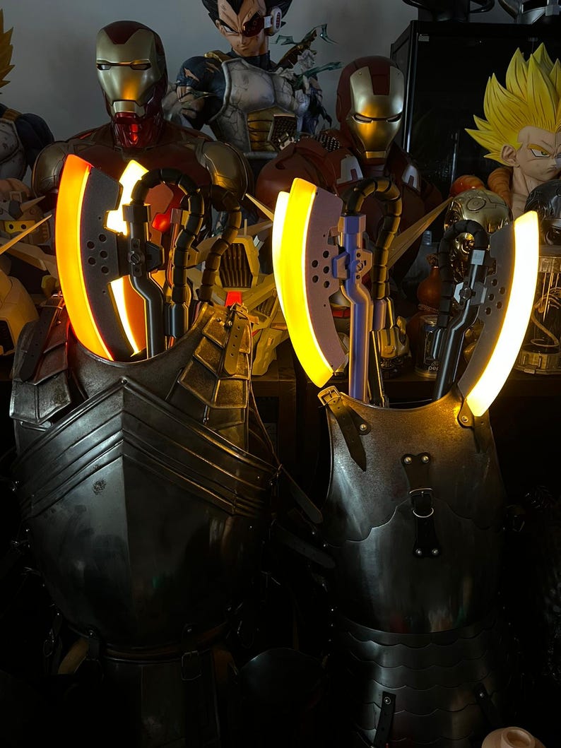 Op de afbeelding: Twee verlichte, metalen pantserstukken met gloeiende gele accenten. Het pantser heeft een donkere, verweerde uitstraling, met zichtbare klinknagels en riemen. De achtergrond bevat verschillende superheldenbeeldjes, waaronder Iron Man en Vegeta.