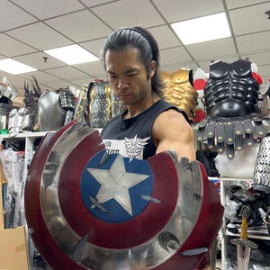 May include: A damaged Captain America shield in red, white, and blue. The shield has a white star on a blue circle, with red stripes and silver detailing. The shield appears to be made of metal.