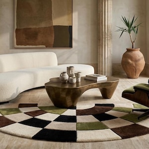 Puede incluir: Un sofá curvo de color crema, una mesa de centro de perfil bajo en tono bronce con tres recipientes de cerámica y una silla de salón con cojín verde oscuro y estructura de madera, sobre una alfombra circular con patrón geométrico negro, marrón y verde.