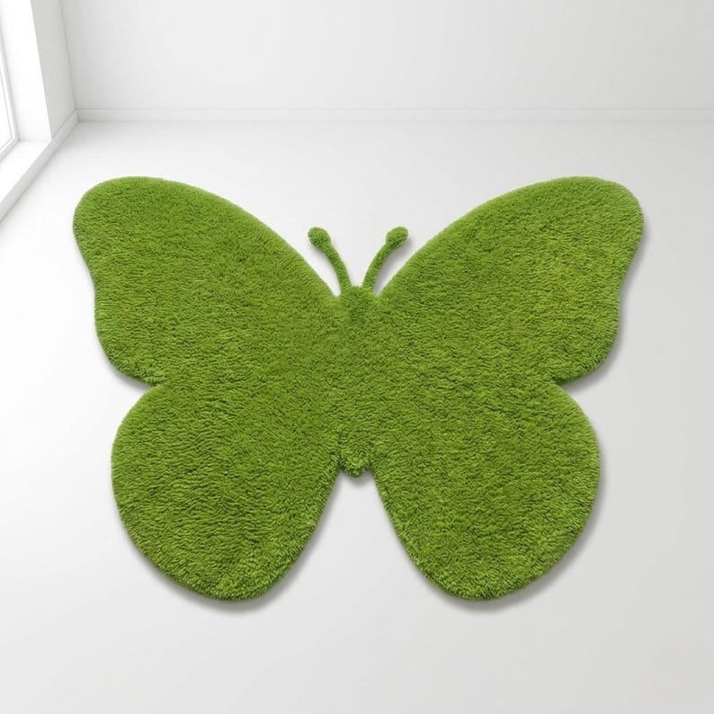 Puede incluir: Una alfombra verde con forma de mariposa con una superficie texturizada y afelpada. La alfombra es de un tono verde vibrante y est&aacute; colocada sobre una superficie blanca. El dise&ntilde;o presenta dos alas grandes y un cuerpo con antenas. Mide unos 150 cm de ancho.