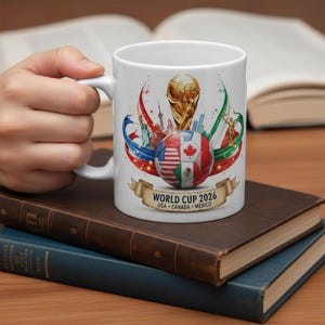 May include: White ceramic mug featuring a colorful design for the 2026 World Cup. The design includes a soccer ball with flags of the USA, Canada, and Mexico, along with the World Cup trophy and the text "WORLD CUP 2026 USA &bull; CANADA &bull; MEXICO".