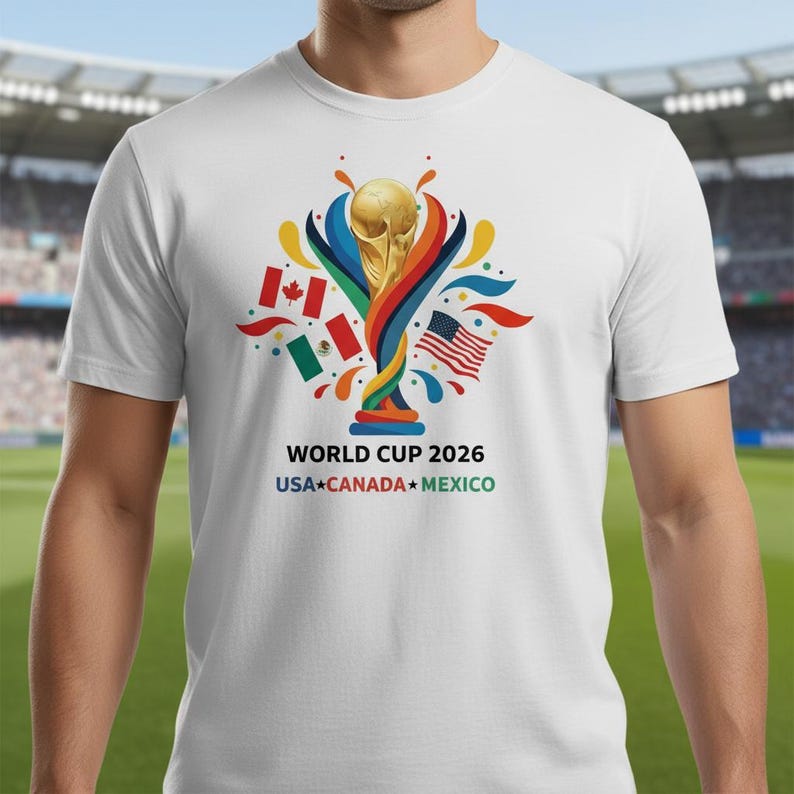 May include: White t-shirt featuring the World Cup 2026 logo with a golden trophy, colorful accents, and flags of the USA, Canada, and Mexico. The text "WORLD CUP 2026 USA CANADA MEXICO" is printed below the graphic.