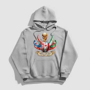 May include: A gray hooded sweatshirt featuring a graphic for the 2026 World Cup. The design includes a soccer ball with flags of the USA, Canada, and Mexico, a gold trophy, and ribbons. The text "WORLD CUP 2026" is displayed on a banner.