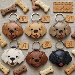 May include: A selection of leather dog keyrings in shades of brown, beige, and black. Each keyring showcases a dog face design with a red tongue and a metal ring. The keyrings are displayed with dog bone biscuits and tags that read "Boho Circle". The tag also reads "Genuine Leather & Hand Stitched".