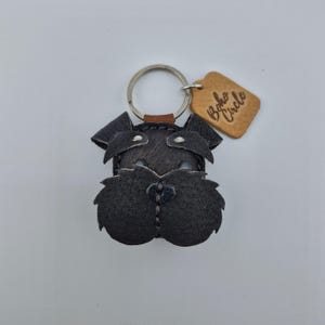 Pu&ograve; includere: Portachiavi in pelle nera a forma di cane Schnauzer, con un portachiavi argentato e un piccolo cartellino in pelle marrone chiaro con la scritta "Boho Circle". Il volto del cane &egrave; dettagliato con cuciture.