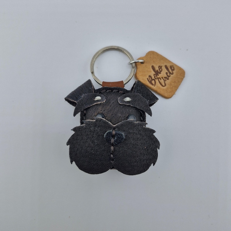 Pu&ograve; includere: Portachiavi in pelle nera a forma di cane Schnauzer, con un portachiavi argentato e un piccolo cartellino in pelle marrone chiaro con la scritta "Boho Circle". Il volto del cane &egrave; dettagliato con cuciture.