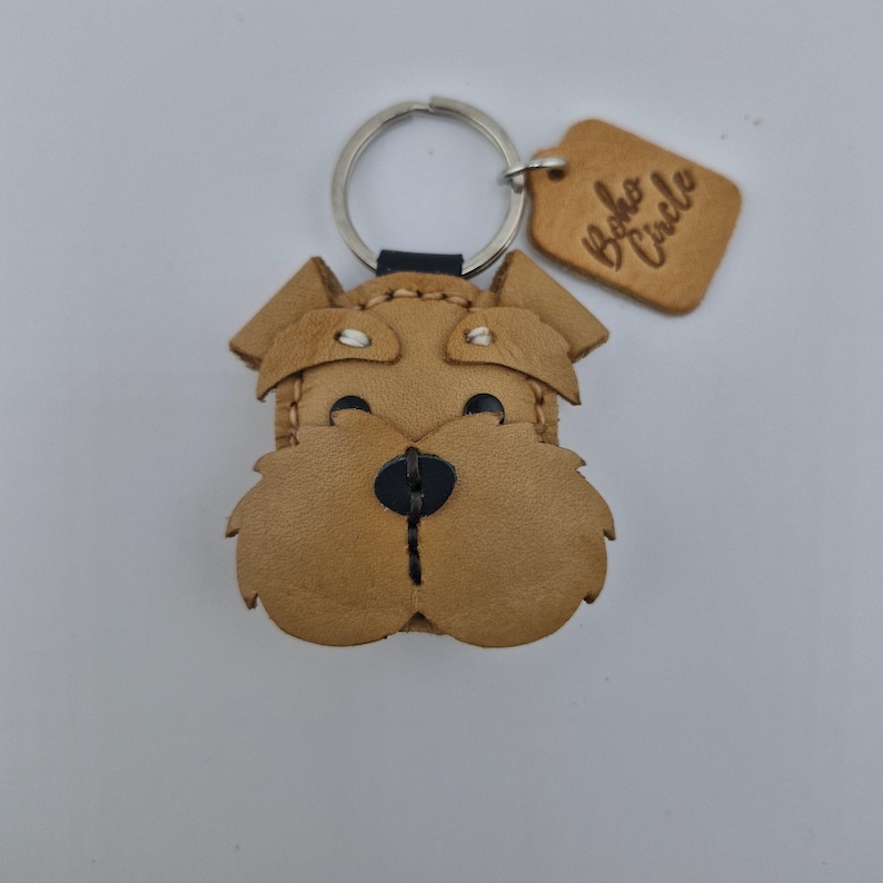Pu&ograve; includere: Un portachiavi a forma di cane in pelle marrone chiaro, con un portachiavi argentato e un piccolo cartellino. Il viso del cane &egrave; dettagliato con cuciture nere per gli occhi e il naso. Il cartellino recita "Boho Circle".