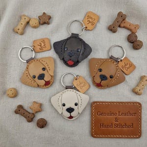 May include: Four leather dog-shaped keychains in black, tan, and cream colours, each with a metal ring and a small rectangular tag labelled Boho Circle. The keychains are surrounded by several bone-shaped and star-shaped dog treats.