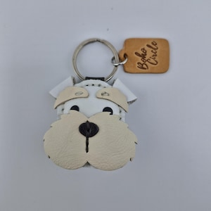 Pu&ograve; includere: Portachiavi a forma di cane in pelle bianca e beige con un portachiavi argentato. Il viso del cane &egrave; dettagliato con occhi neri e un naso nero. Un piccolo tag in pelle beige con la scritta "Boho Circle" &egrave; attaccato al portachiavi.