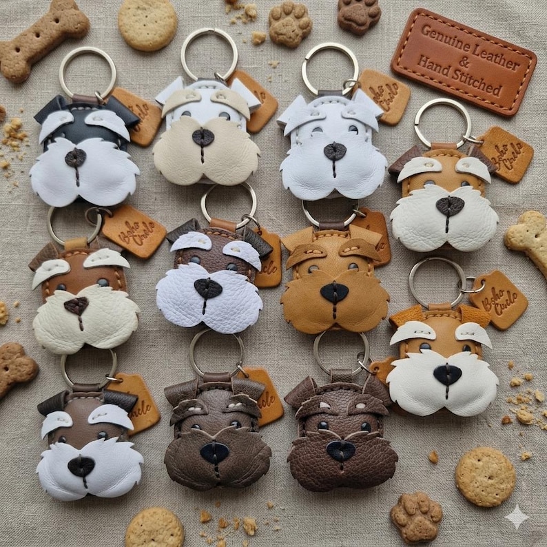 Pu&ograve; includere: Una collezione di portachiavi in pelle fatti a mano a forma di cane, in vari colori, tra cui nero, bianco, marrone e beige. Ogni portachiavi presenta un anello di metallo e una piccola etichetta. I portachiavi sono circondati da biscotti per cani e un'etichetta in pelle con la scritta "Genuine Leather & Hand Stitched".