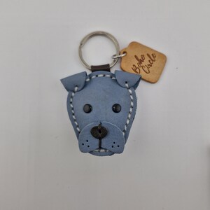 May include: A blue leather dog-shaped keychain with black eyes and a stitched outline. The keychain has a silver ring and a small wooden tag that reads "Boho Circle".
