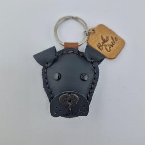 May include: A black leather dog-shaped keychain with a metal ring and a small brown leather tag. The tag is engraved with the words "Boho Circle". The dog's face has black eyes and a stitched nose.
