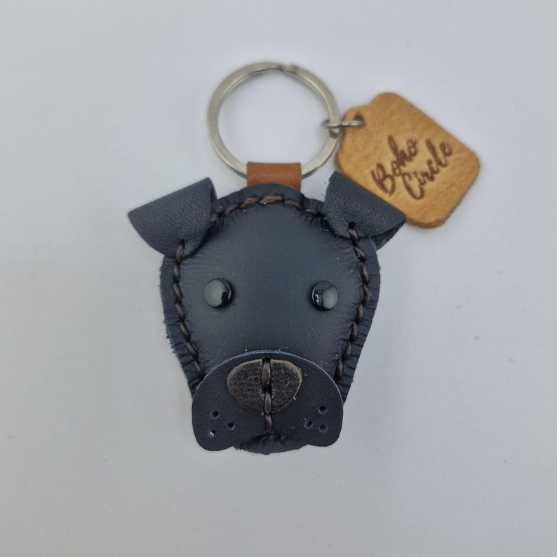 May include: A black leather dog-shaped keychain with a metal ring and a small brown leather tag. The tag is engraved with the words "Boho Circle". The dog's face has black eyes and a stitched nose.
