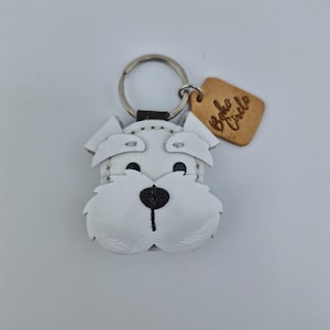 Pu&ograve; includere: Portachiavi a forma di cane in pelle bianca, con occhi e naso neri e bocca cucita in nero. Il portachiavi ha un anello in metallo argentato e un piccolo cartellino in pelle marrone con la scritta "Boho Circle". Il muso del cane &egrave; rifinito con cuciture.