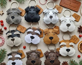 May include: A collection of eleven leather dog-shaped keychains in various colors including gray, black, white, and brown. Each keychain features a metal ring and a small leather tag. A rectangular leather patch reads Genuine Leather & Hand Stitched.
