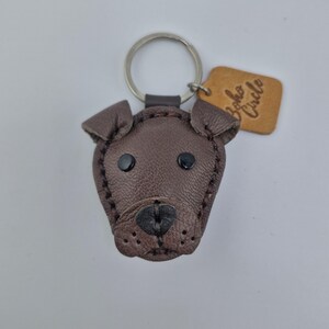 May include: A brown leather dog-shaped keychain with black button eyes and a stitched nose. The keychain has a silver ring and a small, tan leather tag that reads "Boho Circle".