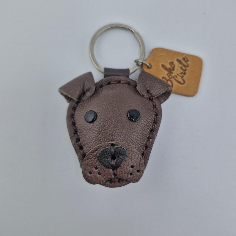May include: A brown leather dog-shaped keychain with black button eyes and a stitched nose. The keychain has a silver ring and a small, tan leather tag that reads "Boho Circle".