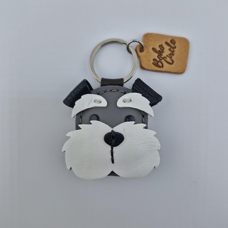 Pu&ograve; includere: Portachiavi a forma di cane Schnauzer in pelle grigia, bianca e nera, con portachiavi argentato. Il portachiavi ha un piccolo cartellino marrone con la scritta "Boho Circle".