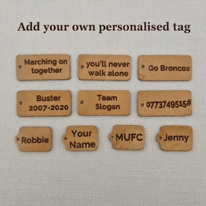 Pu&ograve; includere: Nove etichette rettangolari marrone chiaro con testo inciso come "Marching on together", "Go Broncos" e "Your Name". Ogni etichetta ha un piccolo foro. Il testo "Add your own personalised tag" &egrave; in alto.
